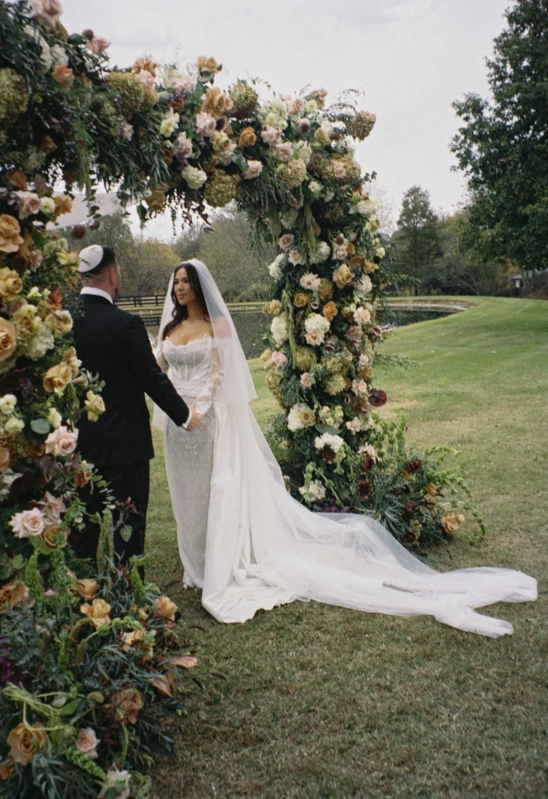 Couple under a garden-rose chuppah beside a pond